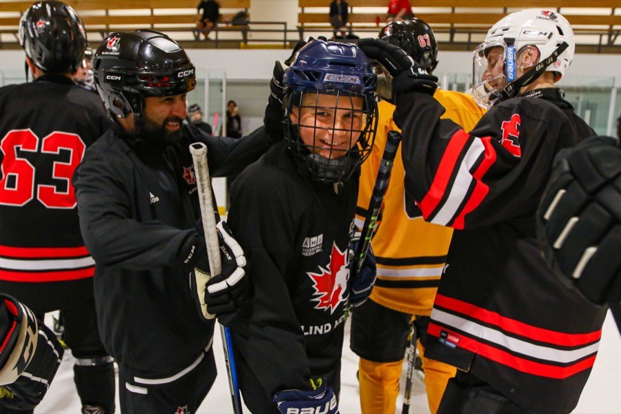 Players in Blind Hockey jerseys huddled together on the bench, smiling