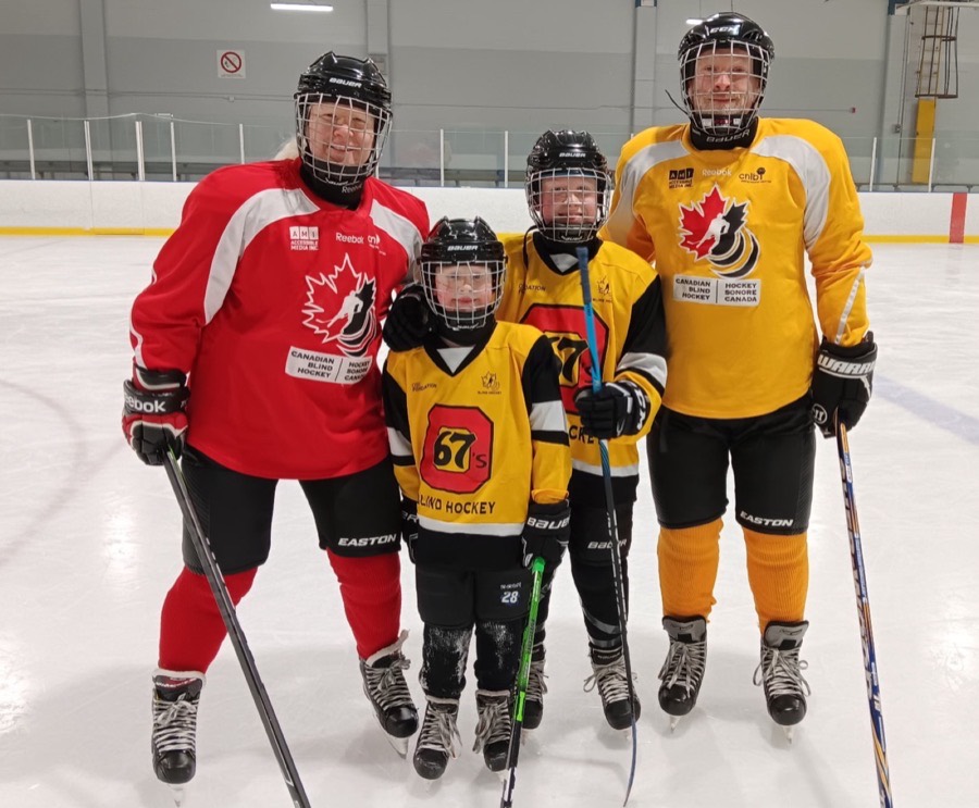 A family of four in Blind Hockey jerseys, two adults and two children, standing together on the ice