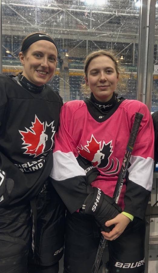 Deux joueuses souriantes près de la bande, l'une en chandail noir du hockey sonore filles et femmes, l'autre en chandail rose de hockey sonore