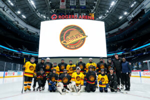 members from the vancouver eclipse smile on the ice infront of the new canucks logo which is displayed on a screen behind them