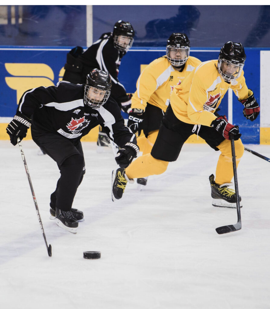two players, one wearing a black jersey and one wearing yellow race to the puck