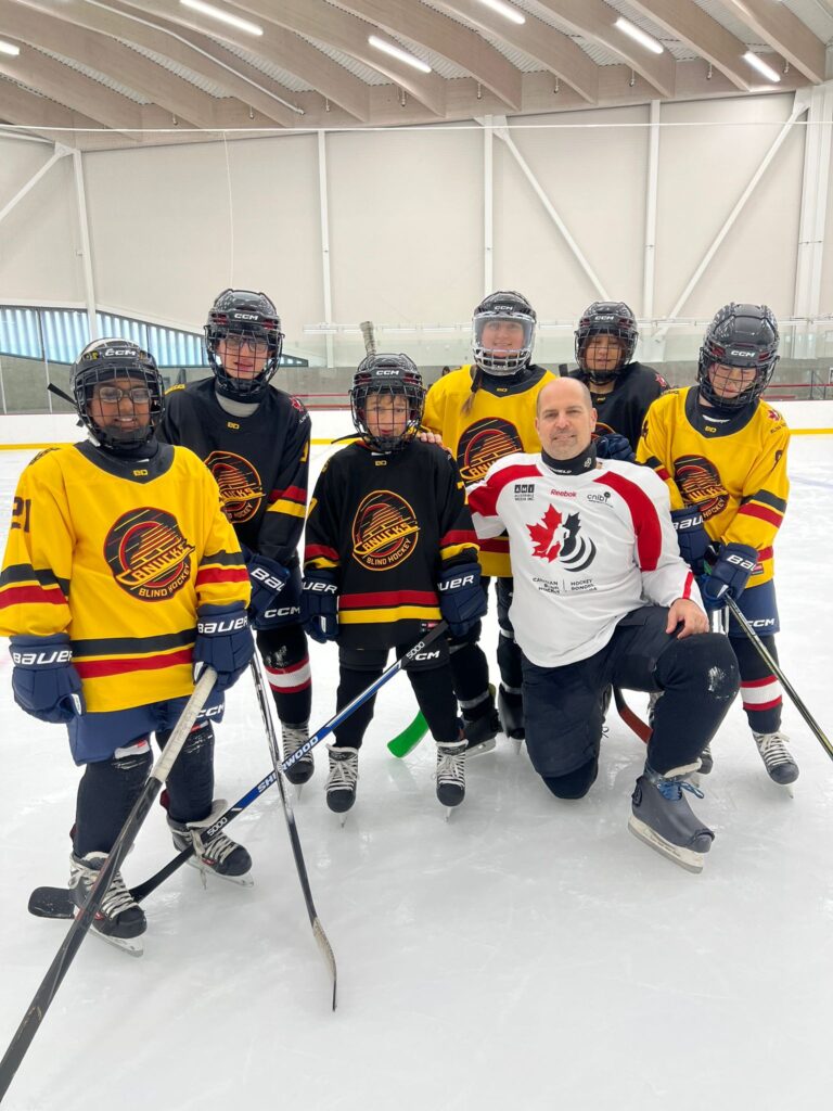Mark kneels beside the Vancouver canucks youth blind hockey team on the ice