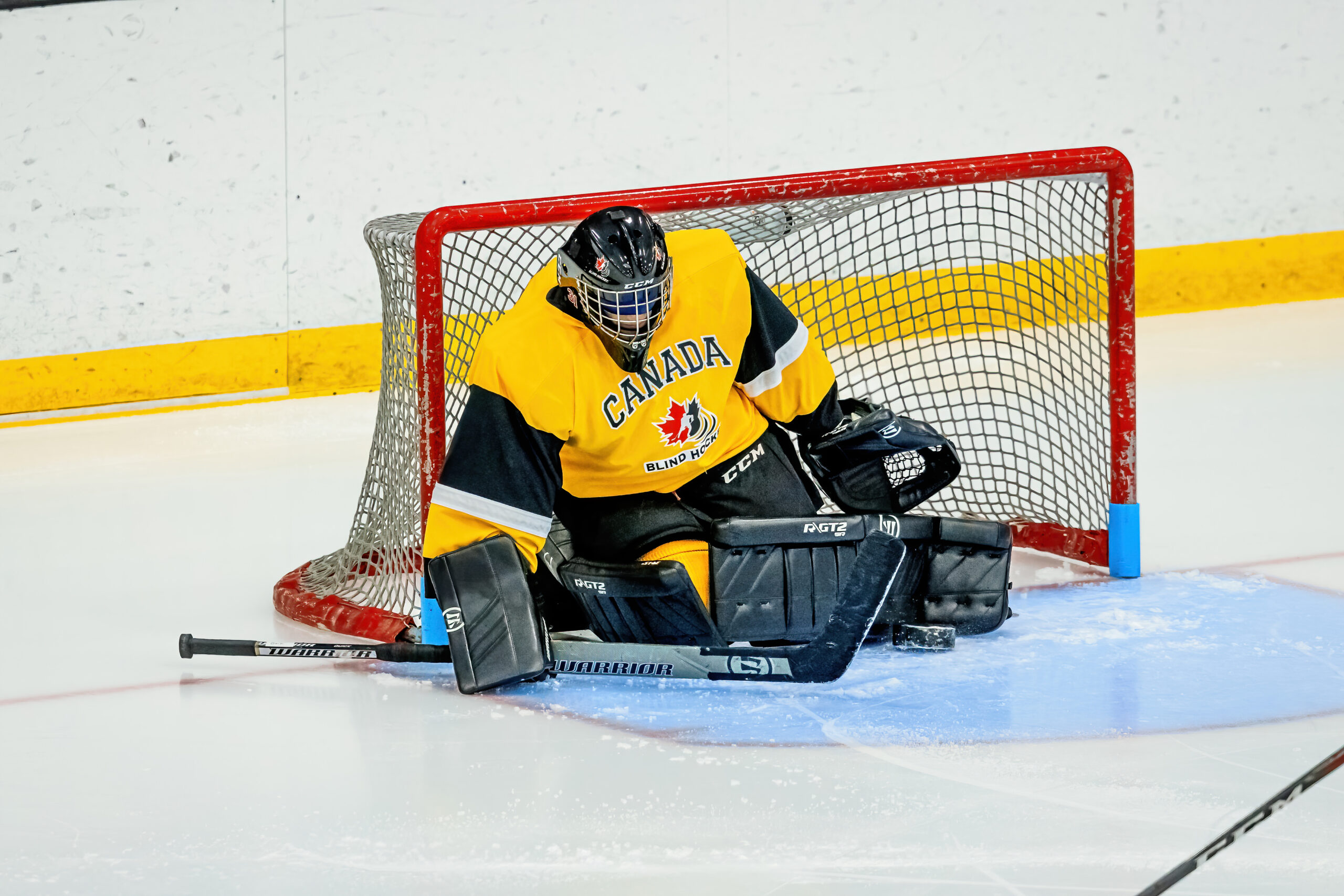 Oliver puck in net for canada attempts to follow the puck in his zone, his blindfold is visible through the cage of the helmet.