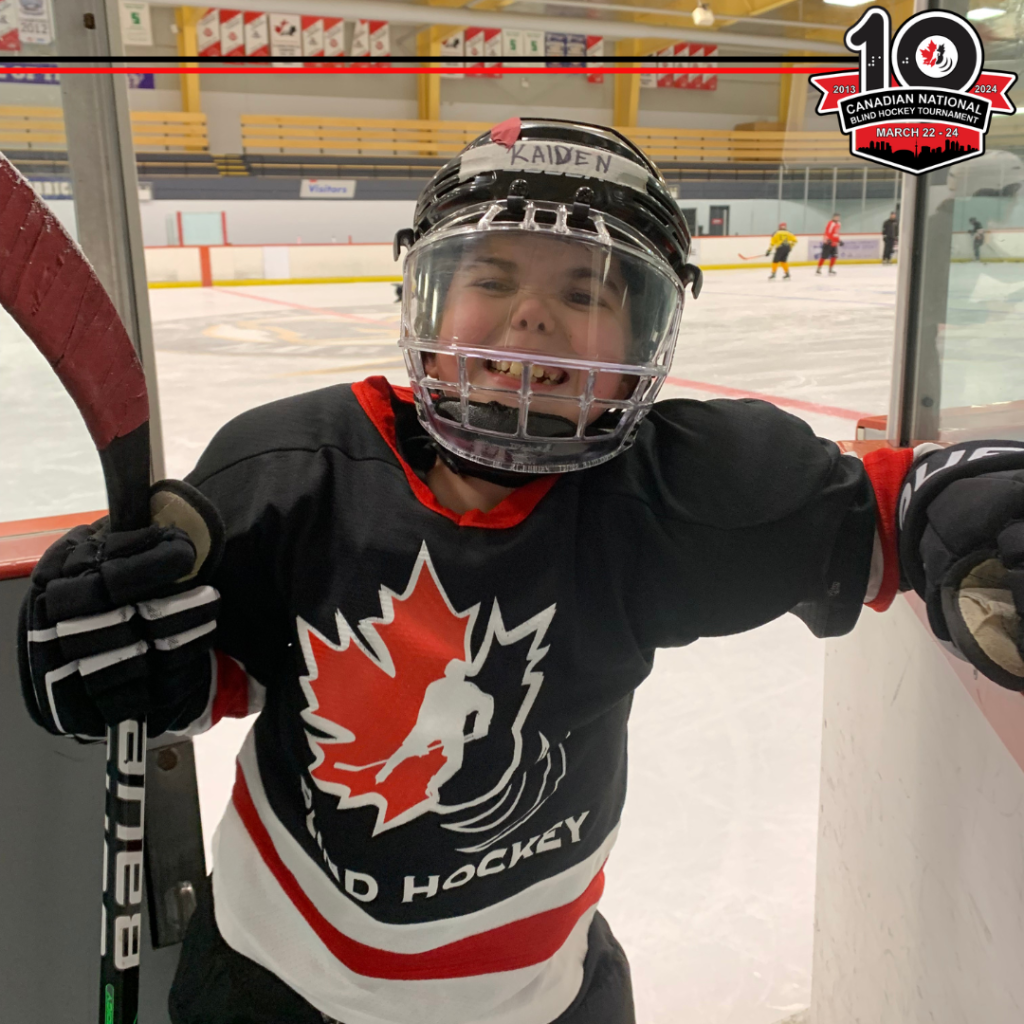 Kaiden has a big smile through the fishbowl of his helmet as he's coming off the ice! There is a black line and a red line at the top of the image leading into this year's logo for year 10